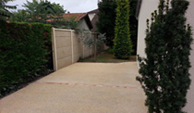 Allée en béton clair le long d'une haie, avec portail et jardin