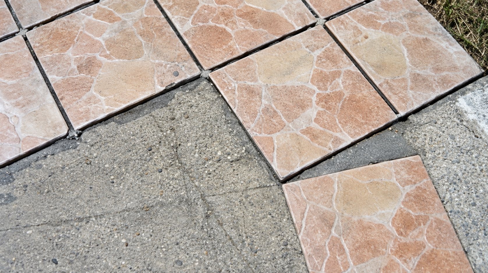 Des carreaux de sol rosés à motifs marbrés sont posés en partie sur une surface de béton gris, avec une zone encore non carrelée.