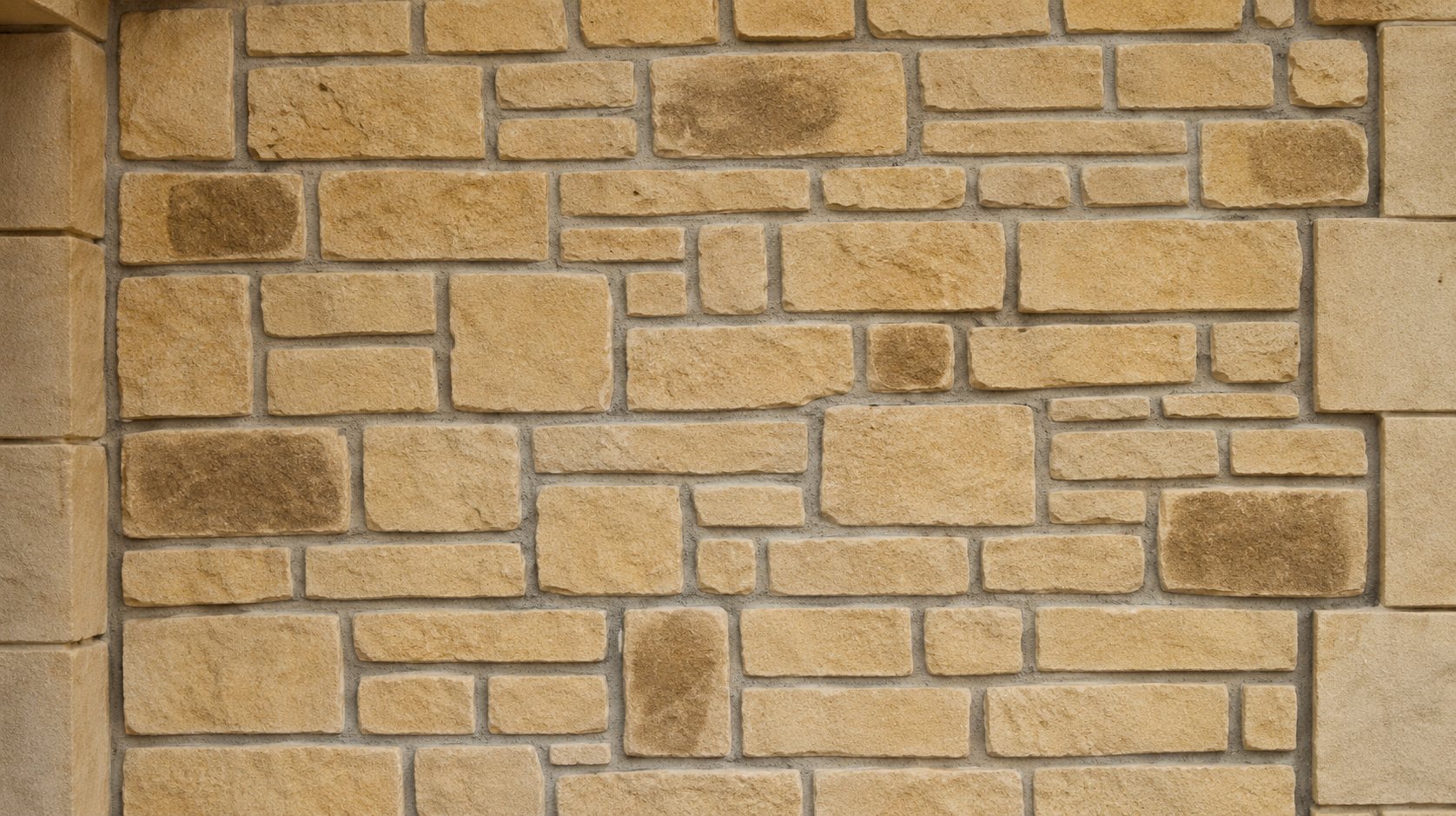 Gros plan sur un mur en pierres de taille beige et ocre, assemblées avec des joints clairs, encadré par deux piliers lisses.